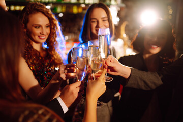 Close up clinking glasses of champagne in the hands of young friends. Happy people celebrating winter holiday together with champagne. Party, celebration, drink, birthday concept.