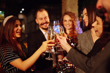 Close up clinking glasses of champagne in the hands of young friends. Happy people celebrating winter holiday together with champagne. Party, celebration, drink, birthday concept.