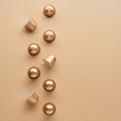 Caffeine, hot drinks and objects concept - close up of golden capsules or pods for coffee mashine on beige background. Top view with space for text. Flat lay..