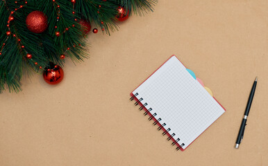 Christmas background with blank notebook, fir branches, decorations on craft paper background. Christmas to-do list or wish list, winter, new year concept. Flat lay, top view, copy space.