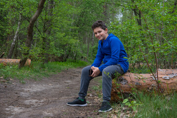 Naklejka na ściany i meble Teen boy sits alone on log in woods and smiles with arms crossed