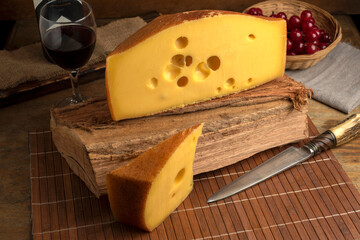 artisan cheeses with dried fruits glass of wine, homemade country bread, bunch of grapes, on wooden board with knife