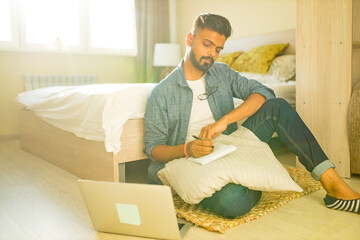 indian bearded male sitting on the floor and making making financial calculations online business in new apartment