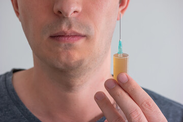 Unidentifiable Caucasian male holding a syringe with orange serum close to his face shallow depth...