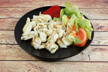 Portion of grilled cuttlefish garnished with lettuce and red pepper, on wooden table