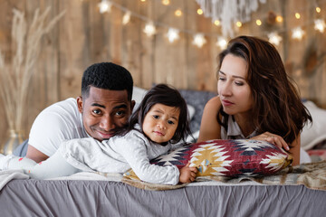 Portrait of a strong happy young family of positive african american dad young mother and mixed race little daughter resting together at home. Positive young family enjoying vacation with each other