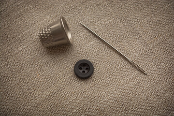 Needle and button close-up. Sewing accessories lie on the fabric in natural warm colors.