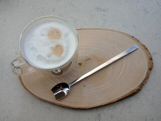 Cappuccino on wooden tray next to long neck spoon.