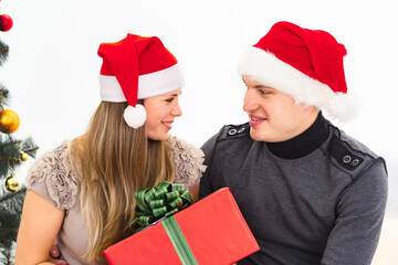 Young couple in christmas santa hats giving a gift on white background