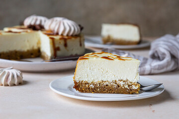 Piece of carrot vanilla cheesecake with salted caramel topping and meringue on a white ceramic plate, light concrete background.