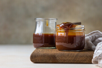 Homemade caramel sauce in a glass jar and spoon on wooden board. Delicious sauce with sea salt for ice cream and desserts.