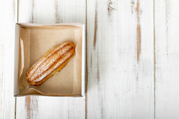 Eclair with cream in a box on a white wooden background.