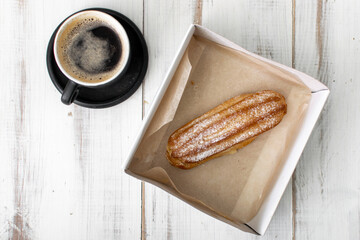 Eclair and coffee cup on a white wooden background.