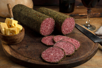 salami, sausages with herbs and cheese cut into slices on wooden board, homemade bread, nuts
