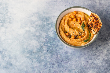 Bowl with homemade hummus garnished with boiled chickpeas, seeds, flatbread and olive oil, blue concrete background. Top view. Copy space. Selective focus.