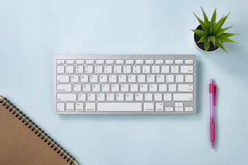White Portable Computer Keyboard Keys or Keyboard Button and Spiral Notebook and Pink Pen and Office Plant on Blue Pastel Minimalist Background