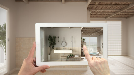 Augmented reality concept. Hand holding tablet with AR application used to simulate furniture and design products in empty interior with ceramic tiles. Bathroom with sink and mirror