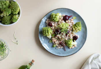 Natural vegan salad of mini beets, romanesco cabbage, white beans and sprouted onion seeds on a gray plate on a light background. Healthy nutrition concept. Selective focus. Top view.