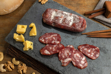 salami, sausages with herbs and cheese cut into slices on wooden board, homemade bread, nuts