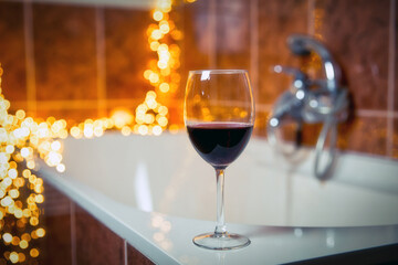 Close up of wine glass with red wine near bathtub with lights on the background, relaxtion and spa concept