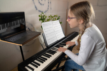 Girl learning to play the piano in distance learning via laptop over the Internet