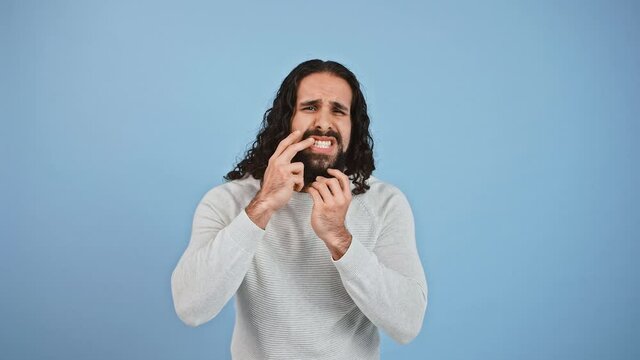 Disappointed bearded guy with long hair checking his hair condition, looking displeased with his appearance
