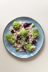 Salad of mini beets, romanesco cabbage, white beans and sprouted onion seeds on a gray plate on a light background. Concept for a vegetarian meal. Selective focus. Top view. Vertical orientation.