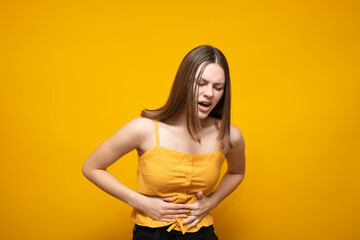 Obraz premium Young beautiful caucasian woman in a yellow tank top on a yellow background with a hand on her stomach because of nausea, painful discomfort. Pain concept.