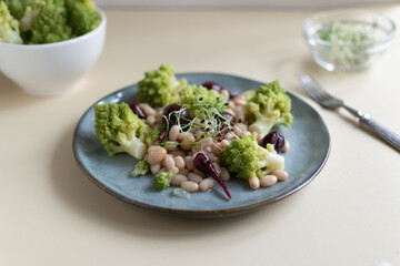 Salad of mini beets, romanesco cabbage, white beans and sprouted onion seeds on a gray plate on a light background. Vagetarian food concept. Selective focus.