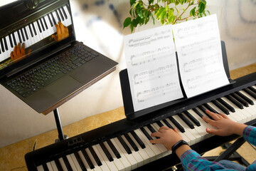 A child learns to play the piano in distance learning via a laptop over the Internet © Anton