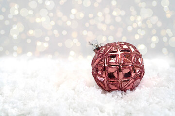 A pink shiny ball for a Christmas tree lies on the white snow. Glass Christmas decoration on a white background. Christmas and New Year atmosphere. Bokeh in the background. Close-up