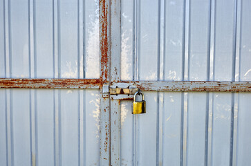 Iron rusty fence with a lock. White corrugated metal or zinc texture surface or galvanize steel in the vertical line background