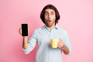 Photo of impressed funny brown hair guy hold cup show telephone wear spectacles blue shirt isolated on pastel pink color background