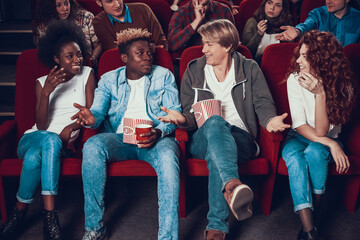 Two friends sit in front row at cinema and talk. 