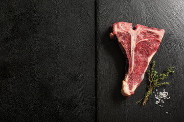 Uncooked Pork T-Bone steak on a stone kitchen cutting board.