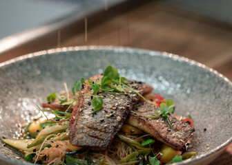 Two pan fried sea bass fillets served on a bed of Asian vegetables and mango, garnished with micro herbs and sesame seeds.
