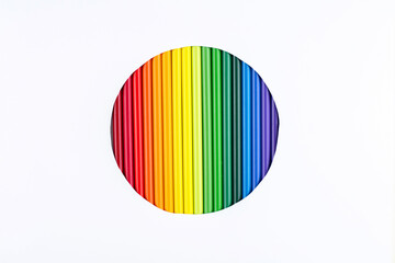 A rainbow of pencils in a cut out circle on a white paper background, closeup, copy space