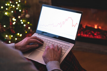 Man freelancer in santa claus hat working on laptop with graphs and charts on screen sitting near...