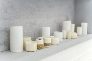 Many white candles on a wooden shelf