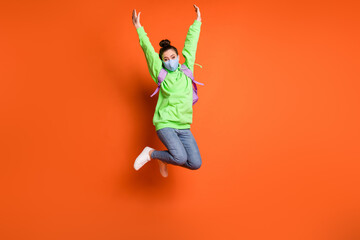Fototapeta na wymiar Full length photo portrait of girl raising hands up jumping wearing blue fabric face mask isolated on vivid orange colored background