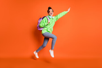 Fototapeta na wymiar Full length photo of careless running young lady dressed green sweatshirt backpack isolated bright orange color background