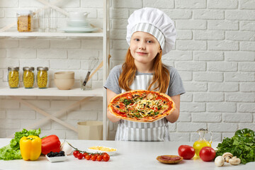 happy little girl in chef hat and an apron cooking pizza in the kitchen. child holding homemade pizza