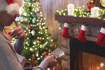 Man counting american dollars sitting near christmas tree and fireplace. Spending money on gift at christmas time. concept. Back view.