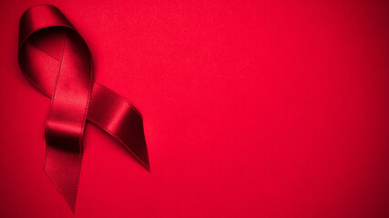 Cancer ribbons. Red ribbon symbol in hiv world day on dark red background. Awareness aids and cancer. Flat lay, top view, copy space