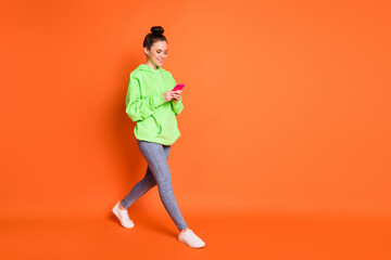 Fototapeta na wymiar Full length photo portrait of woman texting holding phone in two hands walking isolated on vivid orange colored background