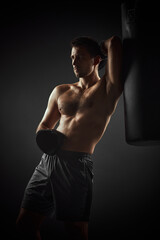 Fototapeta na wymiar shirtless handsome athlete boxer in black gloves standing near punching bag on dark background