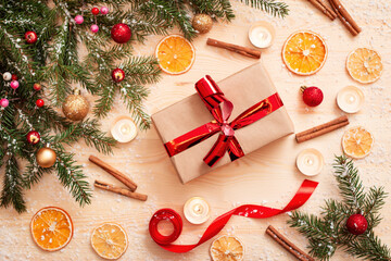 Bright Christmas present box wrapped in parchment paper with red ribbon on wooden table with different decorations. Festive christmas photo