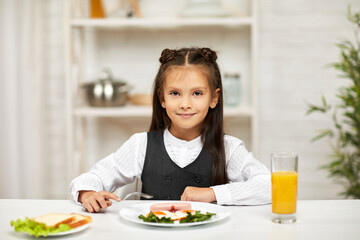 Obraz na płótnie Canvas little child girl having breakfast - fried egg and orange juice in the kitchen. healthy breakfast. fried egg face smiles on a white plate