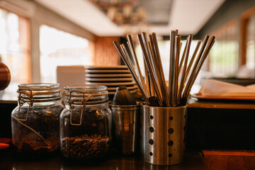 Stainless steel straws in metal jar on kitchen table near pot with coffee beans