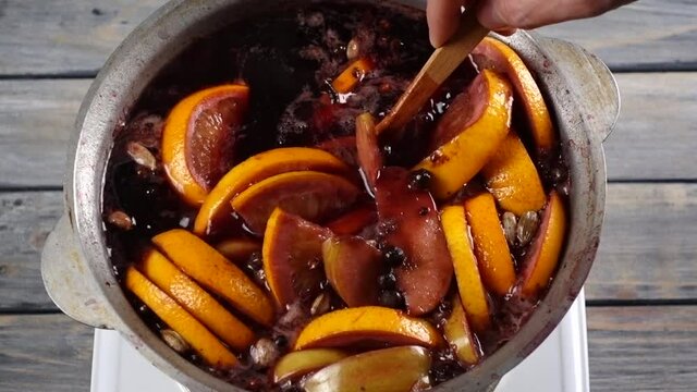 closeup of mulled wine thar stiring wooden spoon, preparing in big old metal kettle at electric stove, above view, slow motion